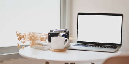 Blank screen laptop in minimal photographer's workplace with vintage camera and coffee cupの写真素材