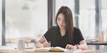 Beautiful Asian freelancer writing her idea in notebook in comfortable working spaceの写真素材