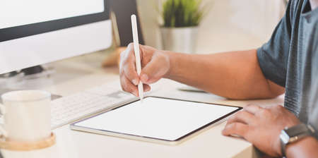 Close-up view of young man using blank screen tablet in modern workplace