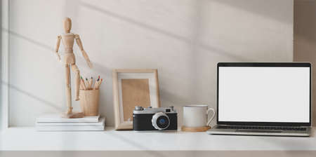 Photographer creative studio with blank screen laptop and office accessories with white wall backgroundの写真素材