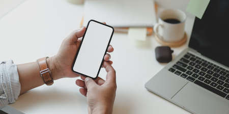 Cropped view of man hand holding blank screen smartphone in modern workplaceの写真素材