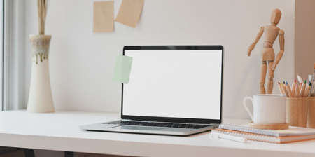 Open blank screen laptop with sticky note note and office supplies on white tableの写真素材