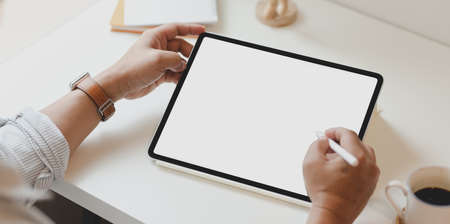 Top view of man using blank screen tablet in minimal office with coffee cup on white desk
