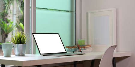 Comfortable workplace with open blank screen laptop and copy space on white desk and open windowsの写真素材