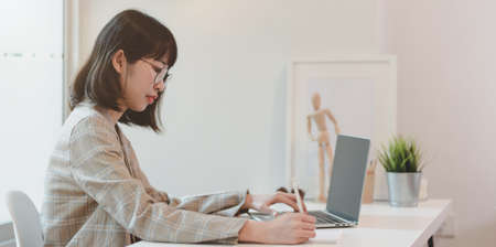 Motivated Asian businesswoman planing her project on laptop while writing the idea on notebookの写真素材
