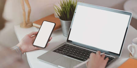 Close-up view of young businesswoman typing on blank screen laptop while holding smartphoneの写真素材