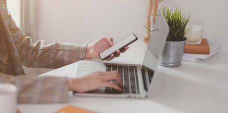 Close-up view of young businesswoman typing on laptop while holding smartphone  in minimal office office styleの写真素材