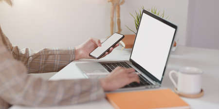 Close-up view of young businesswoman typing on laptop while holding smartphone  in minimal office office styleの写真素材