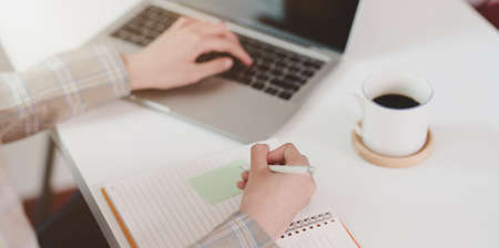 Motivated young businesswoman writing her idea on sticky note while typing on laptop computerの写真素材