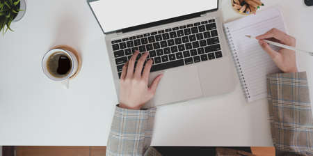 Top view of businesswoman typing on laptop computer and writing her idea on notebook with coffee cupの写真素材