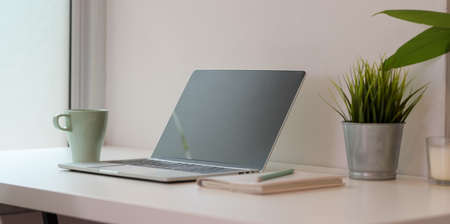 Open blank screen laptop computer with coffee cup and office supplies on white desk in minimal office styleの写真素材