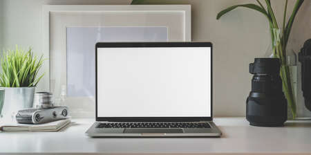 Trendy photographer workplace with blank screen laptop and vintage camera on white tableの写真素材