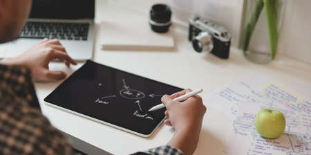 Close-up of young designer drawing mind mapping about his project on tablet in modern office roomの写真素材