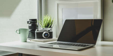 Minimal photographer workplace with laptop, vintage camera and office supplies on white deskの写真素材