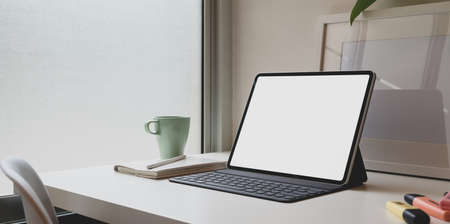 Minimal comfortable workplace with blank screen tablet and cup of coffee on white tableの写真素材