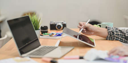 Cropped view of young graphic designer writing his idea concepts on tablet with laptop computer on tableの写真素材
