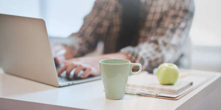 Close-up of young designer working on his project while typing on laptop computer in modern office roomの写真素材