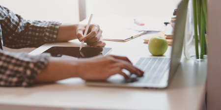 Close-up view of male designer working on his project while typing on laptop and writing on tabletの写真素材