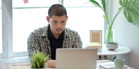 Young professional designer working on his project while using laptop computer in comfortable roomの写真素材