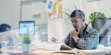 Young male designer working on his project while using tablet in comfortable workplaceの写真素材