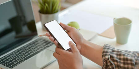 Close-up view of young man holding blank screen smartphone while working with laptop computerの写真素材