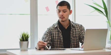 Young male designer working on his project while using laptop computer and tabletの写真素材