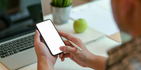 Young man searching on new information on blank screen smartphone while working on tabletの写真素材