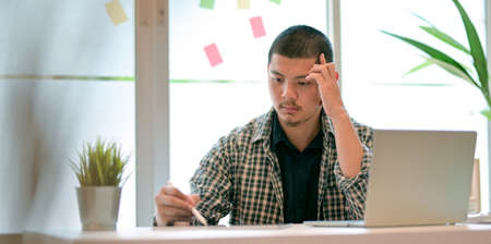 Young male designer working on his project and looking stressful in modern office roomの写真素材
