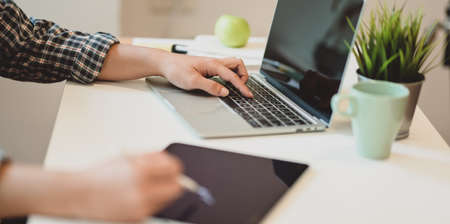 Close-up view of young male freelancer working on concepts while using tablet and laptop computer