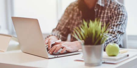 Close-up of young designer typing on laptop computer in modern office roomの写真素材