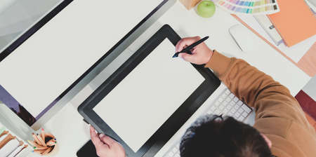 Top view of male graphic designer sketching on tablet with colour swatches and office supplies