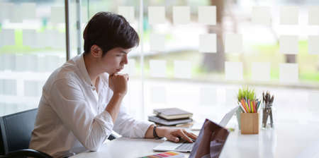 Young professional male graphic designer working on his project with laptop in comfortable office roomの写真素材