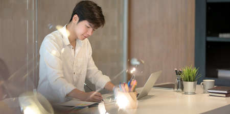 Young professional male graphic designer working on his project in comfortable office roomの写真素材