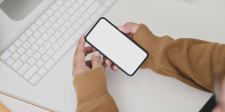 Close-up view of man hands holding blank screen smartphone on table with office suppliesの写真素材