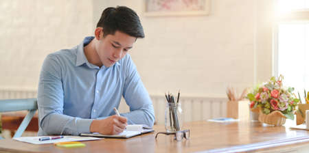 Young professional businessman writing his idea about the upcoming project in notebookの写真素材
