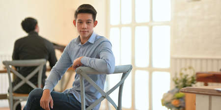 Young professional businessman looking at the camera while sitting on the chair in modern office roomの写真素材