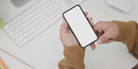Close-up view of man hands holding blank screen smartphone on table with office suppliesの写真素材