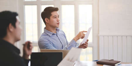 Young professional businessman listening to his coworker presenting their idea in the meeting room