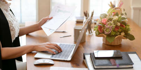 Close-up view of businesswoman working on her project while typing on laptop computer and looking at the paperの写真素材