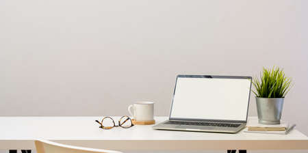 Simple home-office with open blank screen laptop computer and office supplies on white wooden tableの写真素材