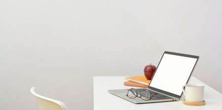 Minimal workplace with open laptop computer and office supplies on white desk and white wall backgroundの写真素材