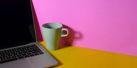 Trendy colourful workplace with laptop computer, coffee cup and book on yellow desk and pink wall backgroundの写真素材