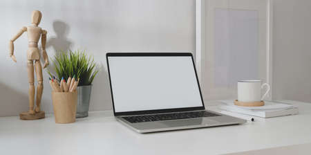 Modern comfortable workplace with open blank screen laptop computer, office supplies and decorationsの写真素材