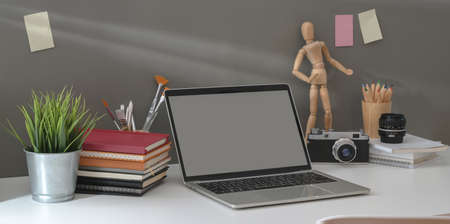 Minimal comfortable workplace with open laptop and vintage camera with decorations on white table and grey wall backgroundの写真素材