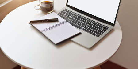 Minimal workplace with open blank screen laptop, open notebook and a cup of coffee on white tableの写真素材