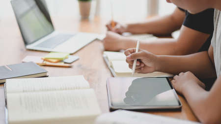 Close-up view of university students discussing their group project while using tablet in comfortable workplaceの写真素材