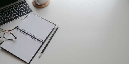 Top view of minimal comfortable workplace with open notebook and laptop with copy space on white table backgroundの写真素材