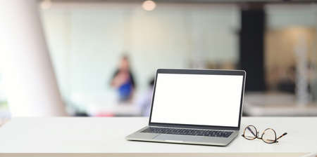 Open blank screen laptop computer and glasses on white desk with blurred backgroundの写真素材