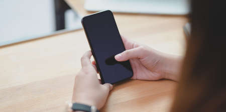 Close-up view of young female holding smartphone on wooden table in comfortable office roomの写真素材