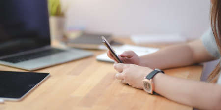 Cropped view of young female freelancer holding smartphone in comfortable office roomの写真素材